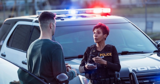 A  policewoman taking a statement from a civilian outside her patrol car.